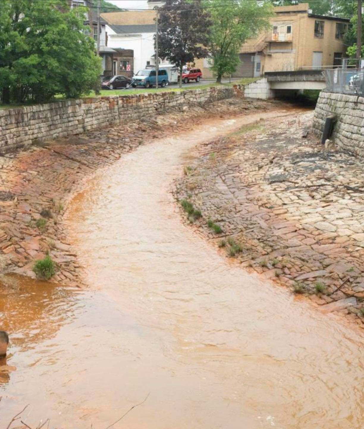 A small stream of orange water, impacted by abandoned mine drainage, flows through the stone-lined channel of Shamokin Creek.